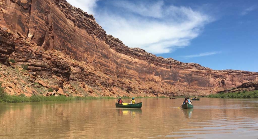 Two canoes are paddled on calm water framed by high canyon walls. 